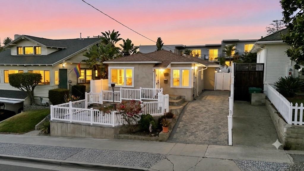 Front elevation of 2036 Lincoln Ave in North Park at dusk, a raised bungalow with a white railing, front corner window and pavered driveway