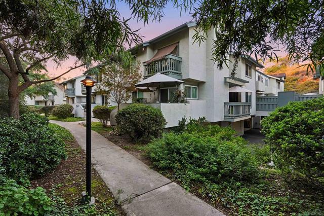 Exterior of 6939 Park Mesa #114 in Linda Vista at dusk, a three-story white townhome with balconies behind lush landscaping and a lamp-lit walkway