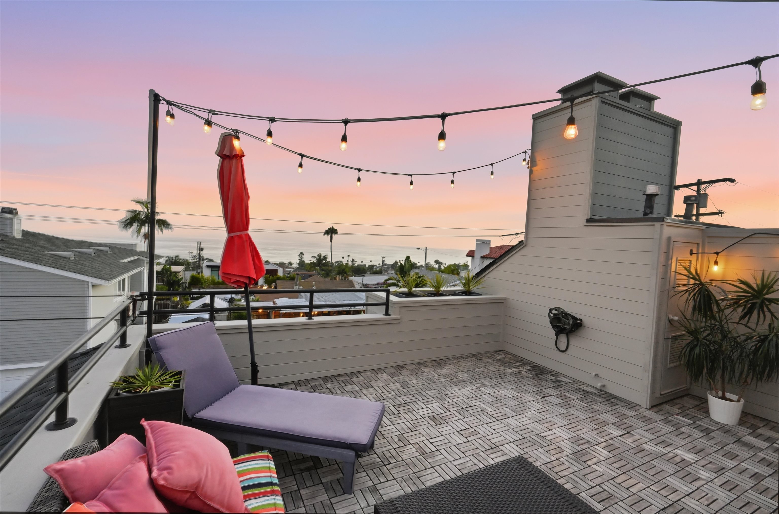 Rooftop deck at 353 Dublin in Cardiff by the Sea at sunset, with string lights, lounge seating and an ocean view over the village